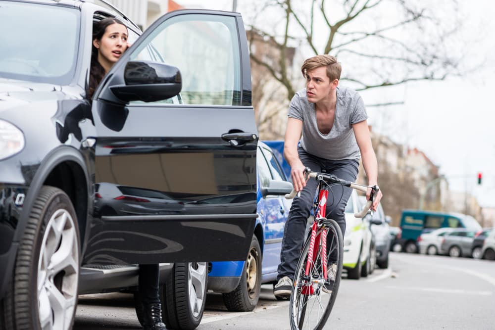 Angry young bicyclist shouting while swerving for avoiding dangerous collision with the open door of a 4x4 car on a busy street in the city